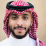 Close-up of Middle Eastern man in dish dash, kaffiyeh, and agal standing outdoors and looking at camera with contented expression.